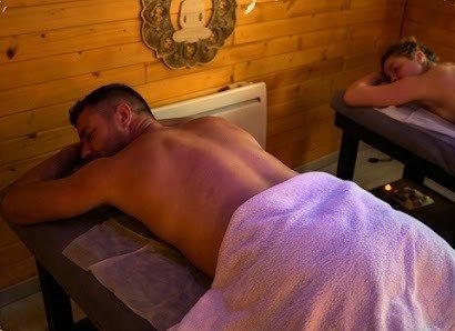 Homme allongé sous une serviette recevant un massage du dos dans la cabine en bois