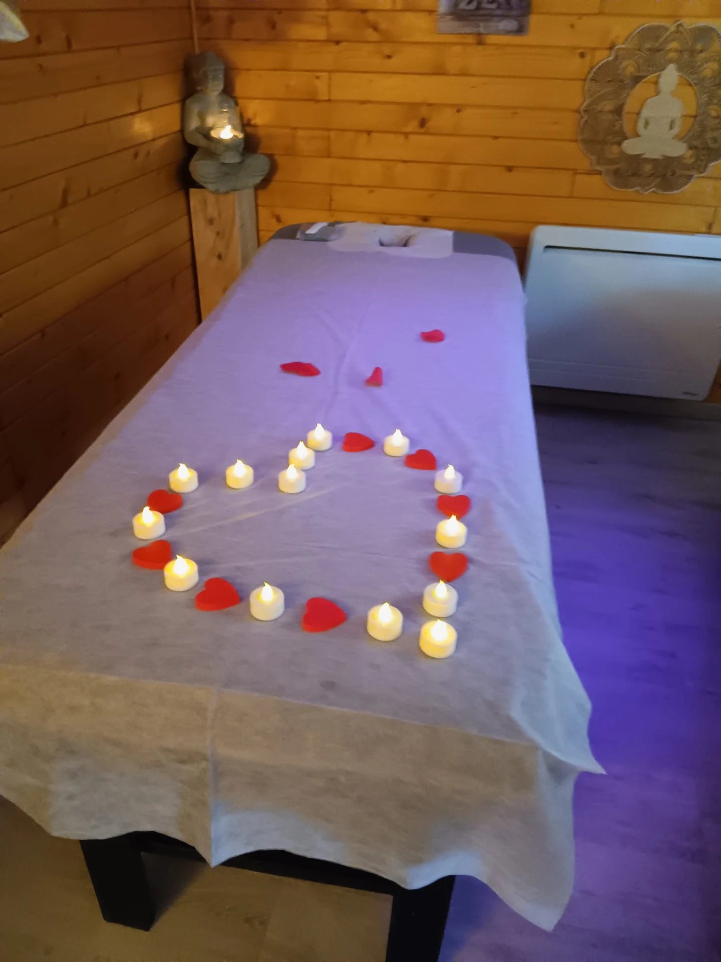 Table de massage décorée de bougies et de cœurs rouges, dans une lumière tamisée